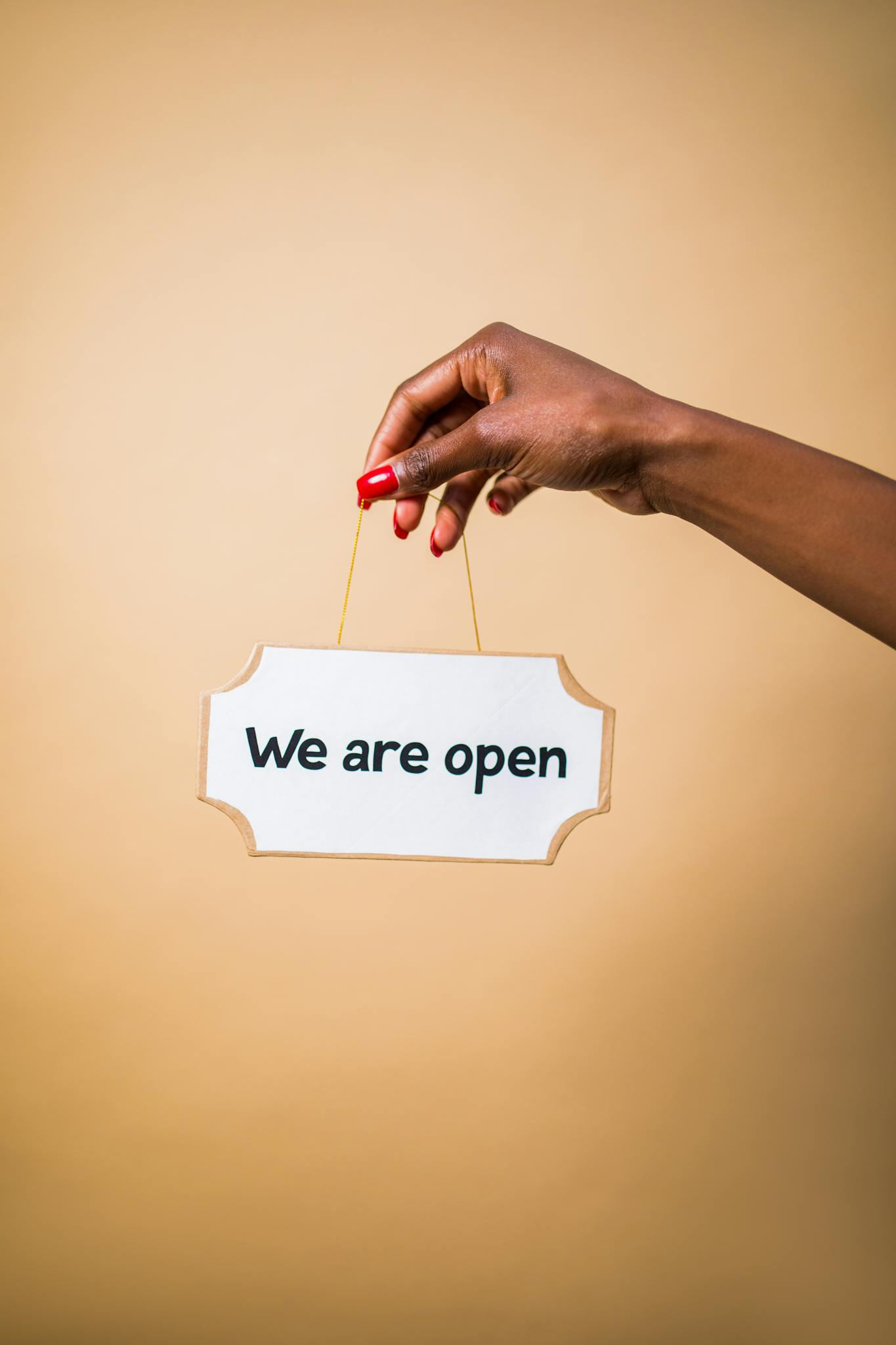 Elegant hand holding 'We are open' sign with a beige background, symbolizing business readiness.